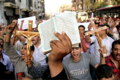 Christian and Muslim demonstrators, some holding the holy Muslim book and others holding the cross, marching in Cairo.