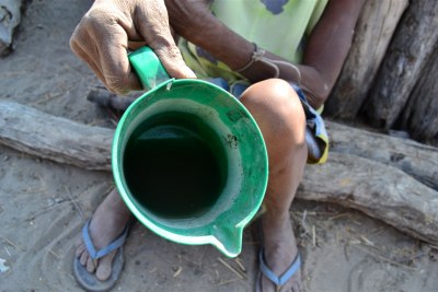 Victoria Nditondino holds up a jug of the dirty, brown water that her grandchildren have drawn from a distant well in southern Angola.
