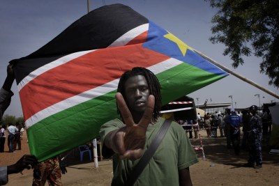 Emmanuel Jal, artiste sud-soudanais, ancien enfant-soldat et activiste politique, posant devant le drapeau de son pays.