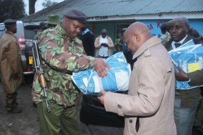 An administration police officer helps a school principal carry KCSE examination papers at Gilgil Sub-County offices in Nakuru on November 13, 2017.