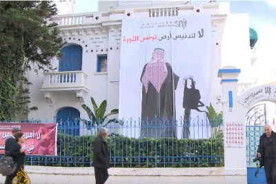 Video screenshot of a poster hung on the office building of the Tunisian Journalists' Syndicate depicting Saudi Prince Mohammed bin Salman holding a chainsaw with the phrase 'no to the desecration of Tunisia, land of the revolution'.