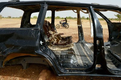 A man on a motorcycle drives by a burnt-out car in the northern region of Burkina Faso in June 2019.